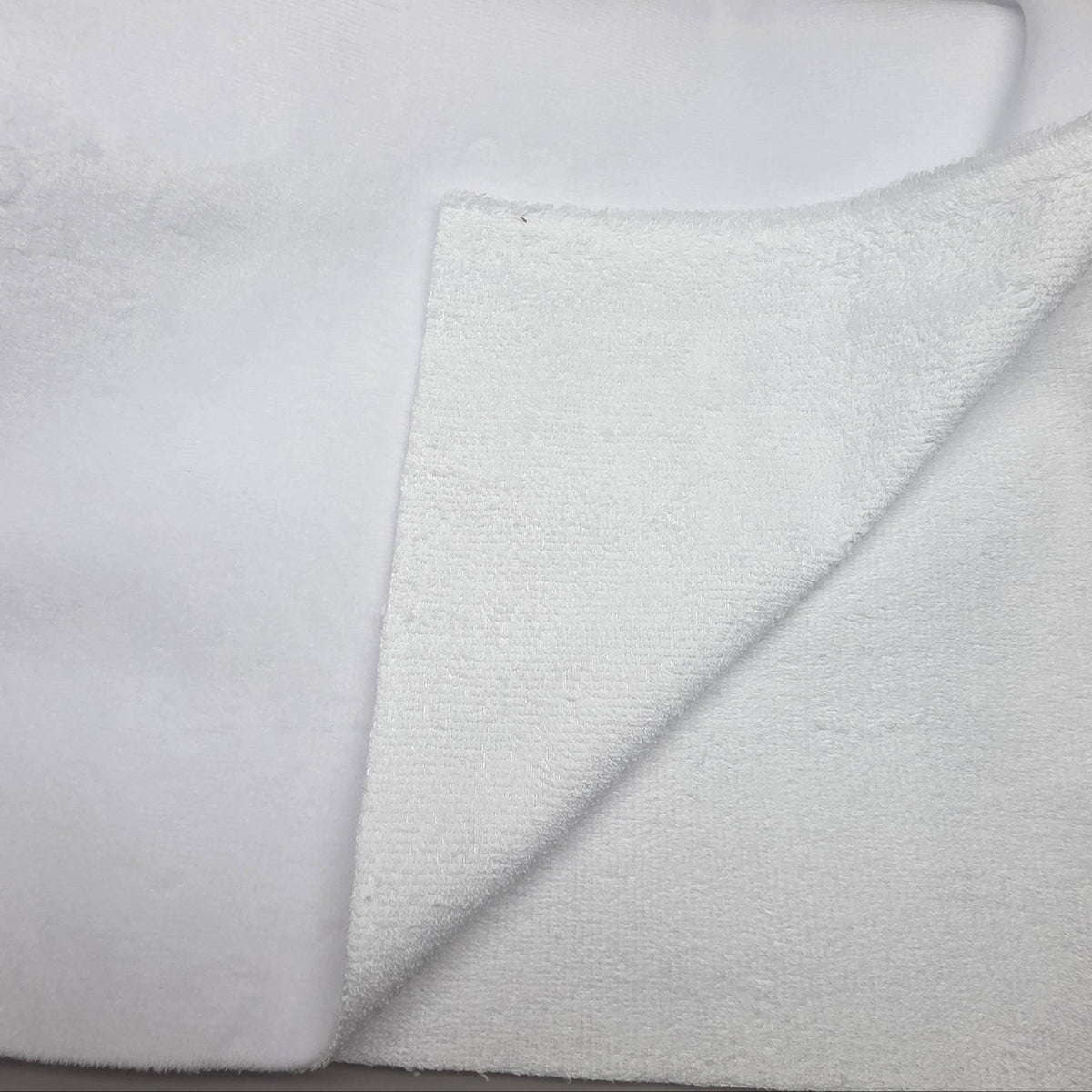 A close-up of a folded white terry cloth towel or blanket, showing the soft textured fabric on both sides against a neutral light gray background.